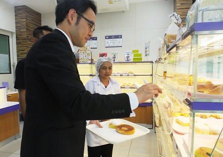 Mr. Kimura sampling 60 Plus+ Bakery & Cafe products with assistance from a staff with disability